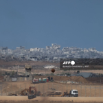 An Israeli military armoured vehicle is transported on the back of a truck along the Israel-Gaza border on October 9, 2025. Israel and Hamas on October 9 agreed a Gaza ceasefire deal to free the remaining living hostages, in a major step towards ending a war that has killed tens of thousands of people and unleashed a humanitarian catastrophe. (Photo by Ahmad GHARABLI / AFP)